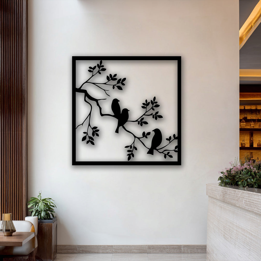 A plant, a table with a lamp, and flowers on a counter complement the Birds on Branch Frame decorative metal art.