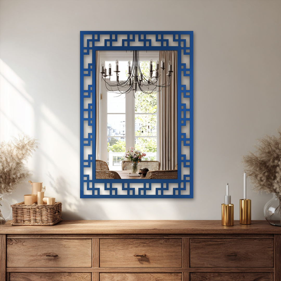Reflected in this modern mirror, a dining room scene is layered with a chandelier, table setting, and garden view, adding depth behind the framed geometric design.