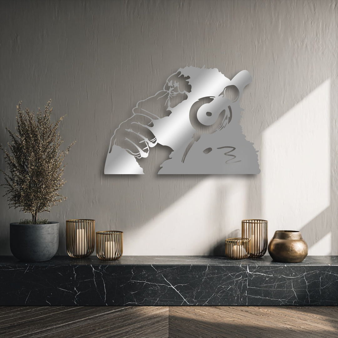 The gleaming silver urban monkey headphones metal artwork stands out against a textured wall, reflecting light, with candles and a plant below.