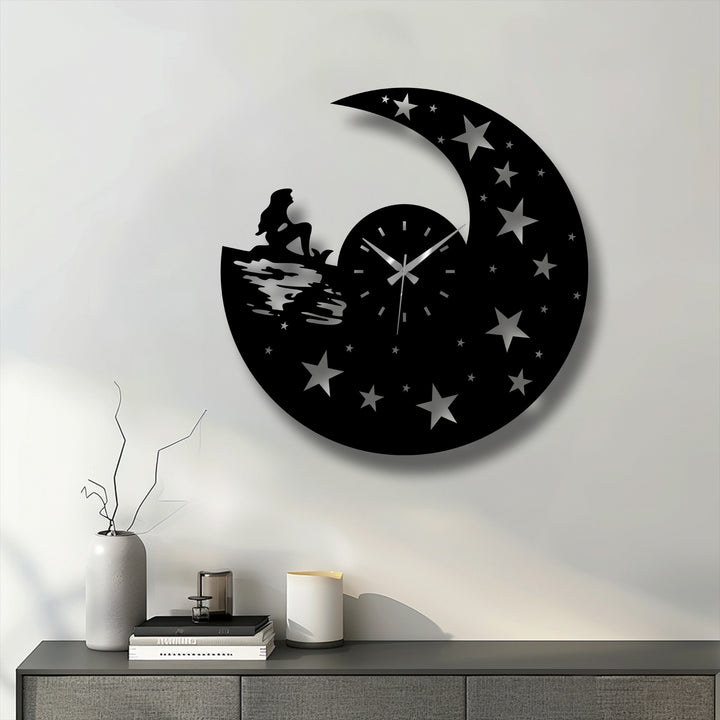 Horizontally oriented circular metal artwork wall clock features a celestial night design with a crescent moon, stars, and a mermaid silhouette.