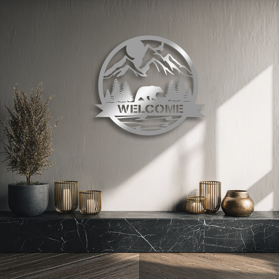 The softest element, a wispy dried plant, stands beside a unique metal wall art piece featuring a mountain bear welcome sign.