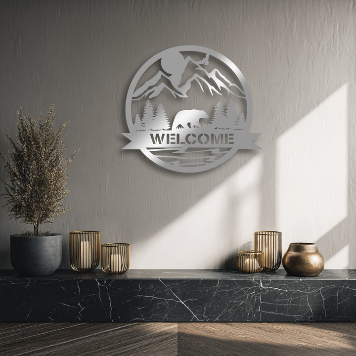 The softest element, a wispy dried plant, stands beside a unique metal wall art piece featuring a mountain bear welcome sign.