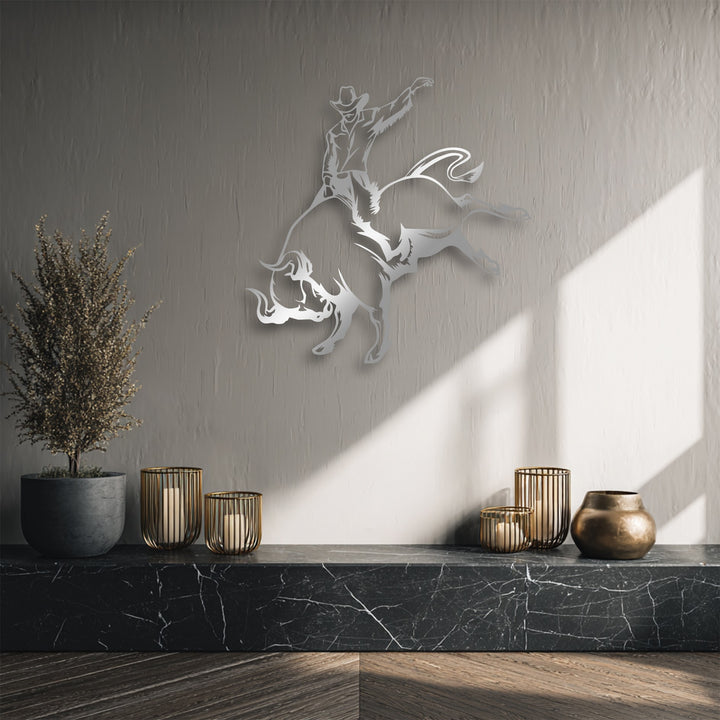 The textured light gray wall serves as the backdrop for the striking cowboy bull riding metal art for wall, illuminated by natural diagonal sunlight.