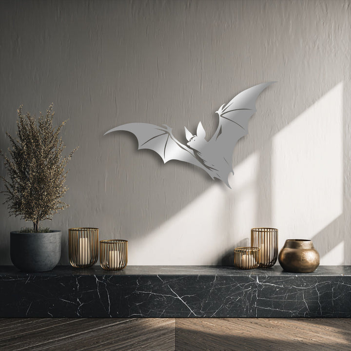 The bold silver flying bat silhouette metal wall decor loudly stands out against the textured gray wall, illuminated by bright natural light.