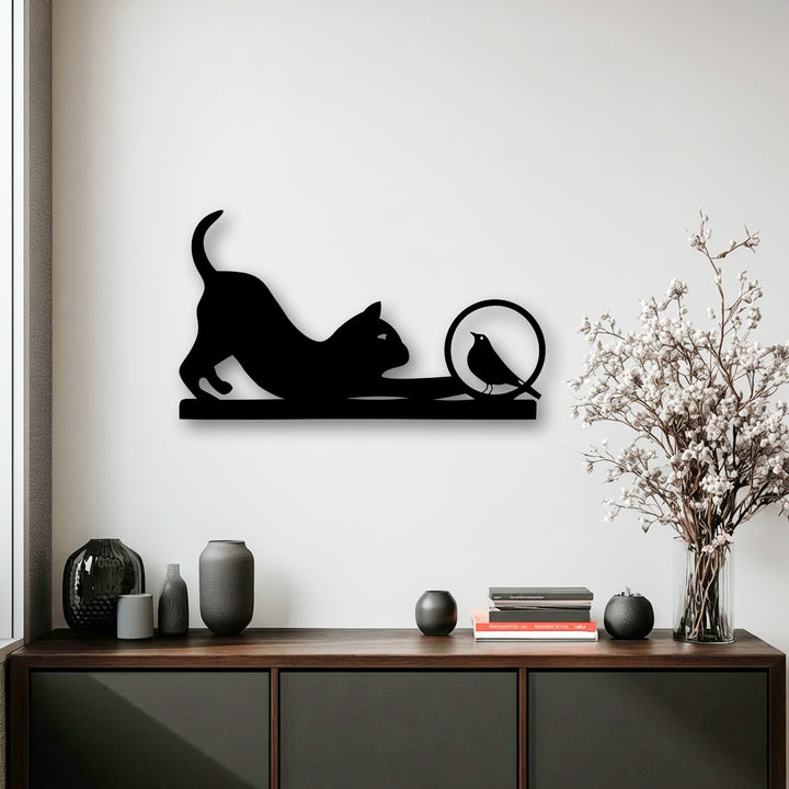 Low color saturation defines the scene, emphasizing a striking unique metal wall art of a playful cat and curious bird silhouette.