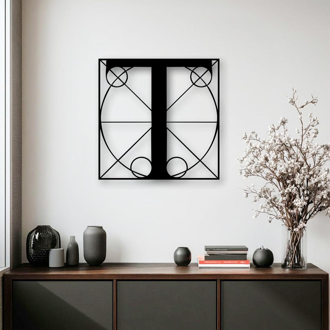 A pristine white wall serves as a minimalist backdrop for a sleek black geometric letter T decorative metal art piece.