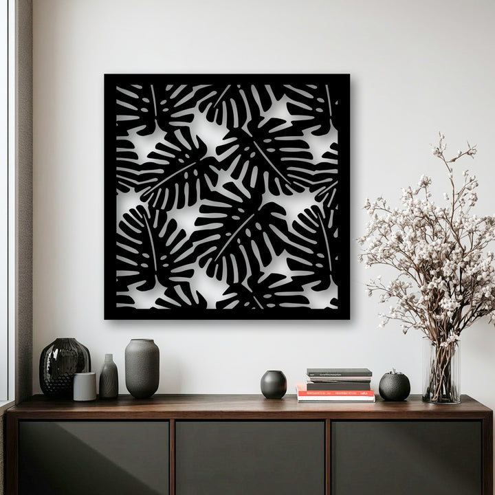 The bright white background highlights the intricate tropical monstera leaf pattern of the decorative metal art.
