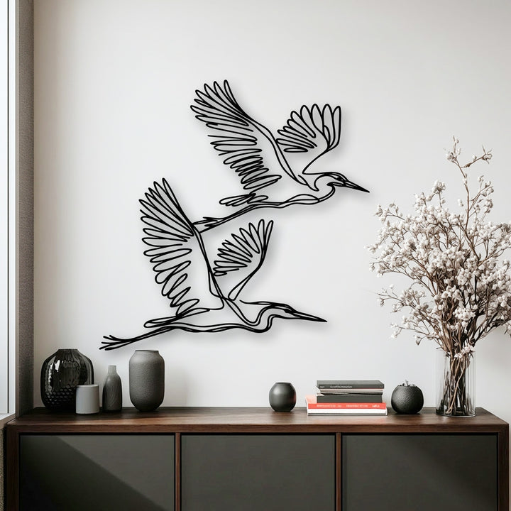 Sleek vases and books on a dark credenza define the foreground, enhancing the unique metal wall art of flying herons above.