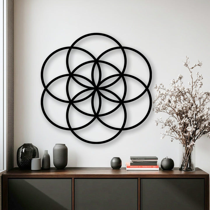 The darkest area showcases the prominent black Flower of Life geometric metal wall decor above a dark brown cabinet.