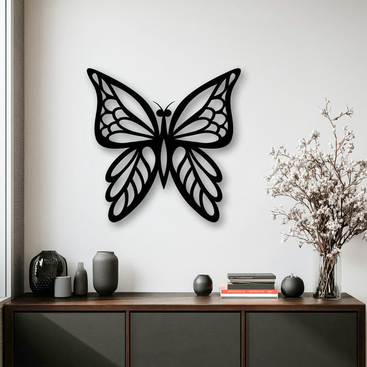 Dark vases and white flowers on a wooden cabinet form the foreground beneath the elegant butterfly metal wall decor.