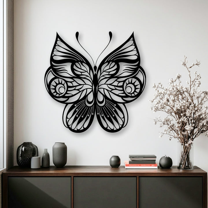 Delicate white blooms in a clear vase complement the striking ornate butterfly metal wall decor above a dark wooden cabinet.