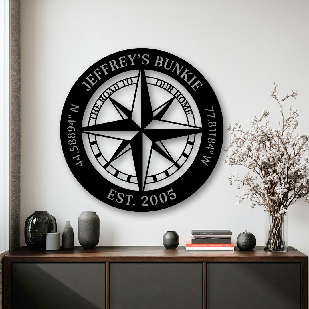 The large, circular black metal art for wall prominently displays a personalized compass with 'JEFFREY'S BUNKIE' and coordinates.