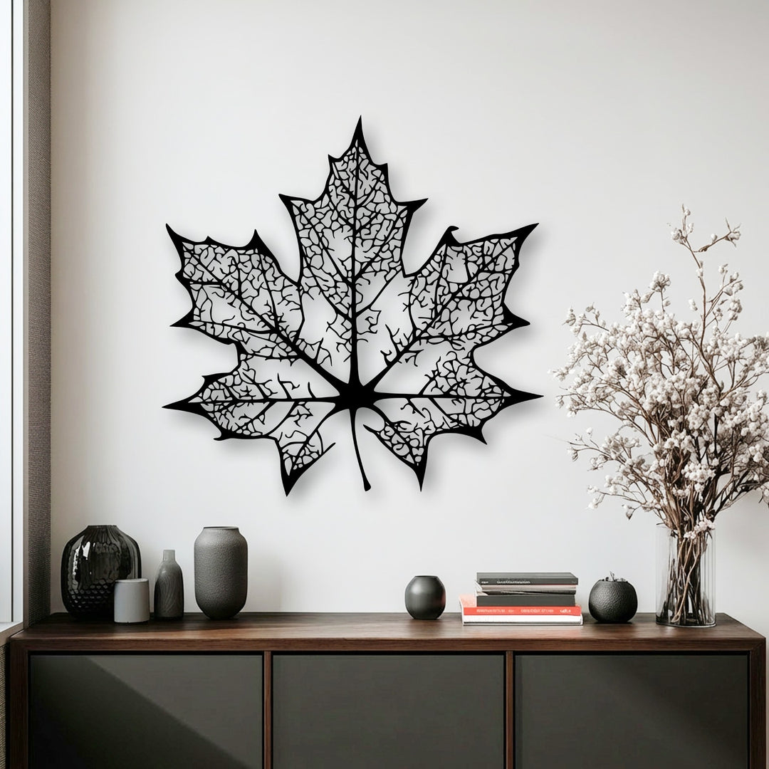 Dark credenza with various vases and books acts as foreground, enhancing the intricate maple leaf silhouette decorative metal art.