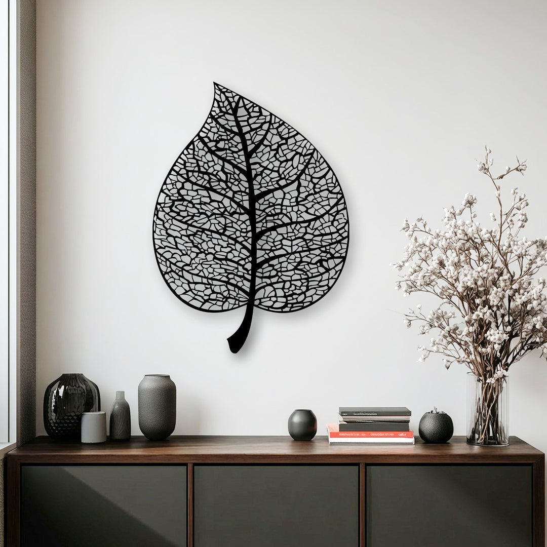 A sharp color transition from the white to the black intricate botanical leaf silhouette metal wall decor and dark wood.