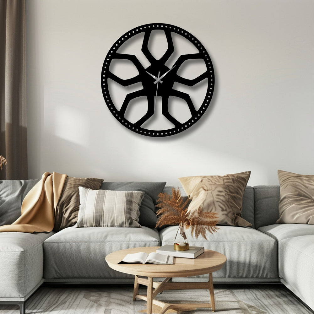 A perfectly circular piece of metal artwork features an abstract radial geometric design, creating a contemporary metal wall clock.