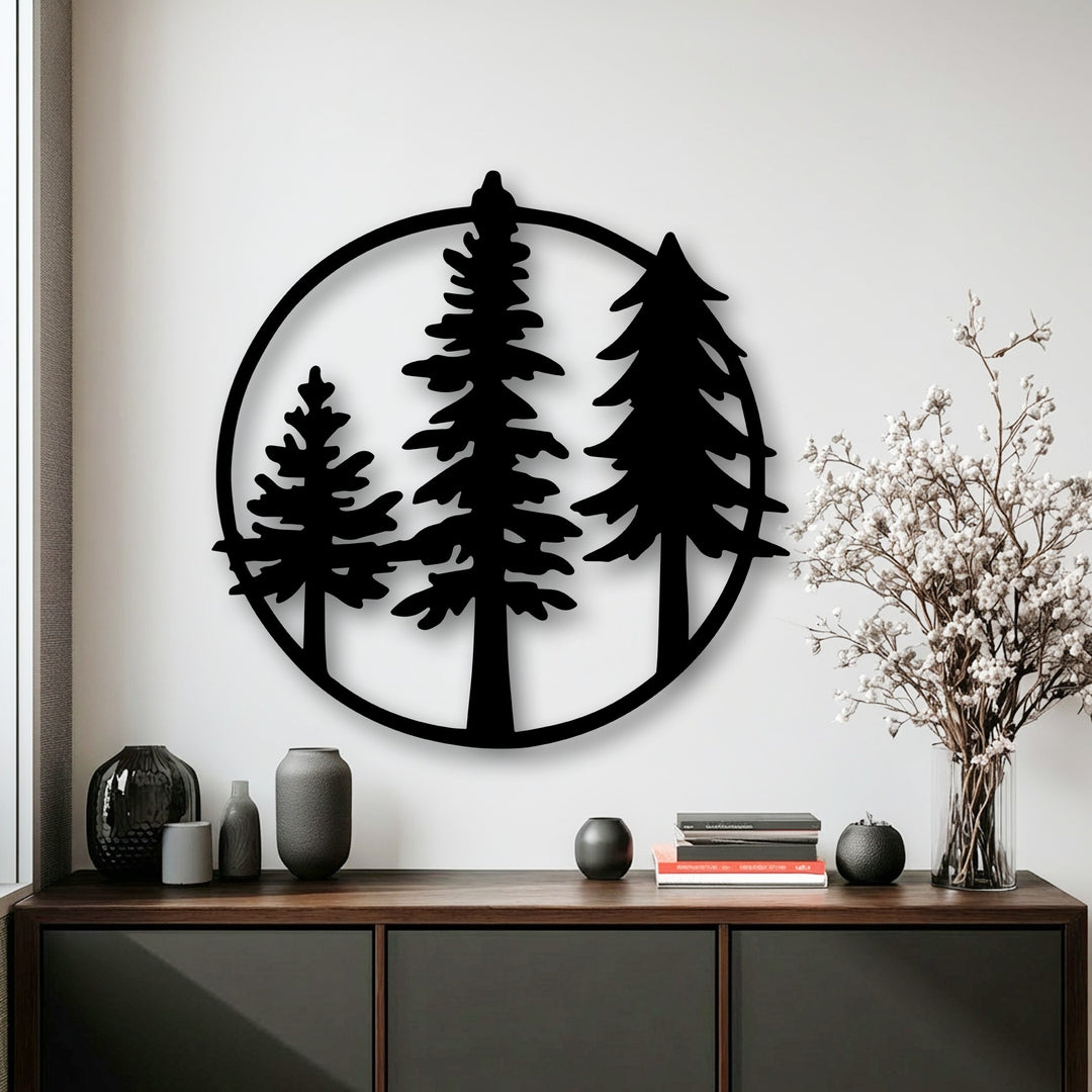 The negative space within the black circular Evergreen Circle metal artwork distinctly outlines three minimalist pine trees against a bright white wall.