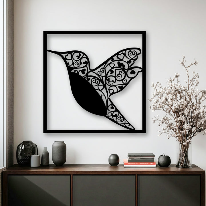 With low color saturation, this metal artwork of a black hummingbird with heart details stands out on a white wall with desaturated decor.
