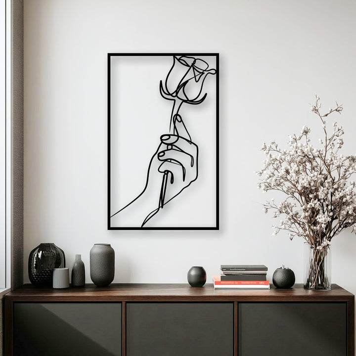 An elegant minimalist metal art for wall showcases a black line art design of a hand gracefully holding a rose.