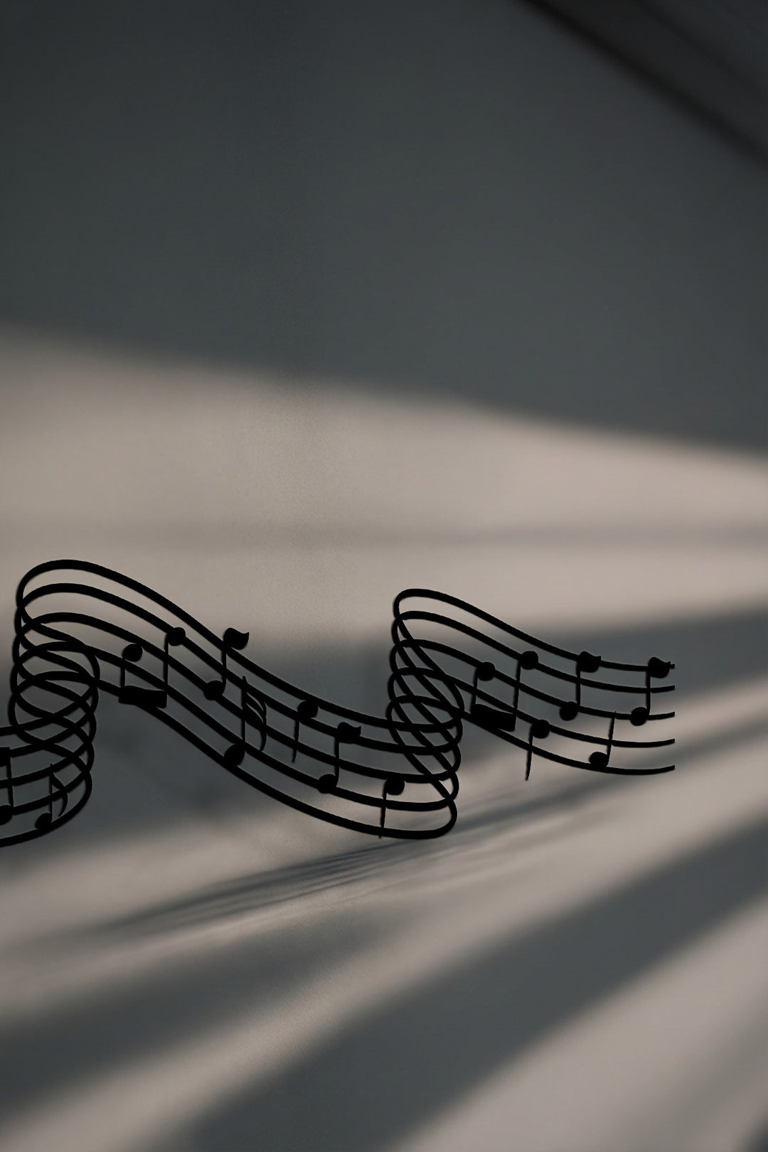 Abstract flowing musical notes, rendered as unique metal wall art, cast dynamic shadows, creating a compelling visual melody on a light surface.