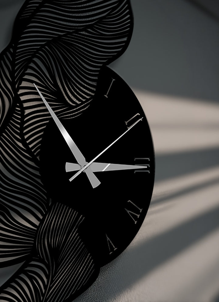 Gleaming silver hands contrast against the striking black face of a decorative metal art wall clock, featuring abstract wavy patterns and crisp Roman numerals.