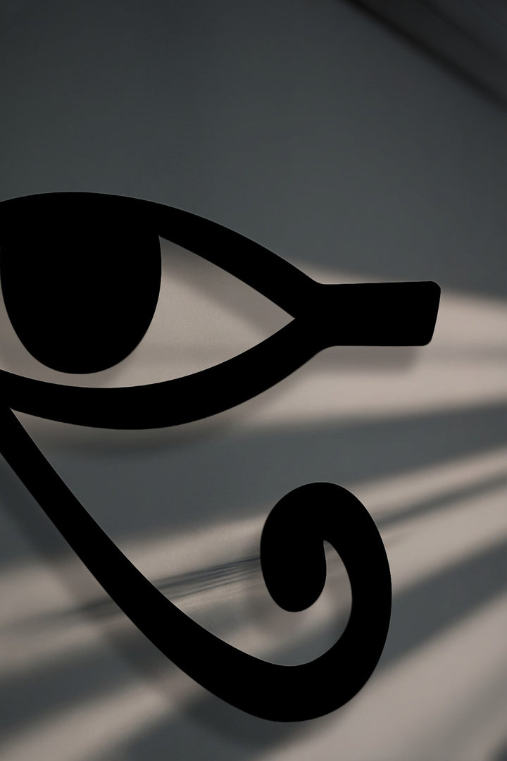 The intricate, crisp borders of the black Eye of Horus metal wall decor cast soft shadows on a subtly textured grey surface.