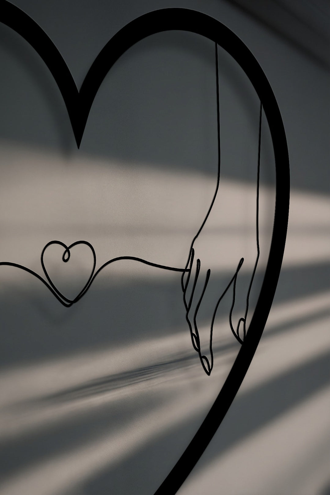 Minimalist black unique metal wall art featuring two hands connected by a delicate heart string, all framed within a large heart shape.