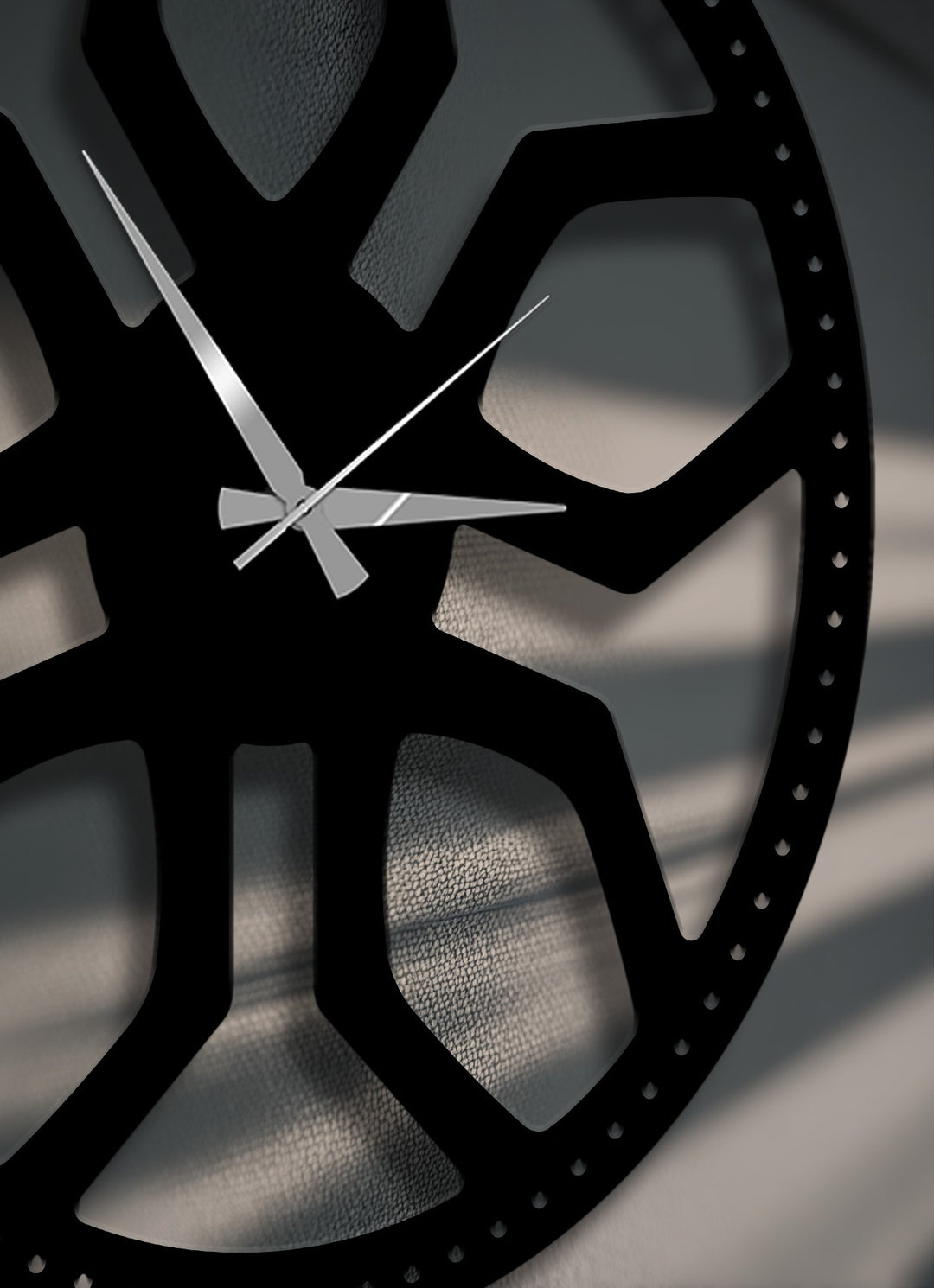The textured, light gray wall behind the unique metal wall art clock features subtle shadows from ambient lighting, highlighting its modern geometric design.