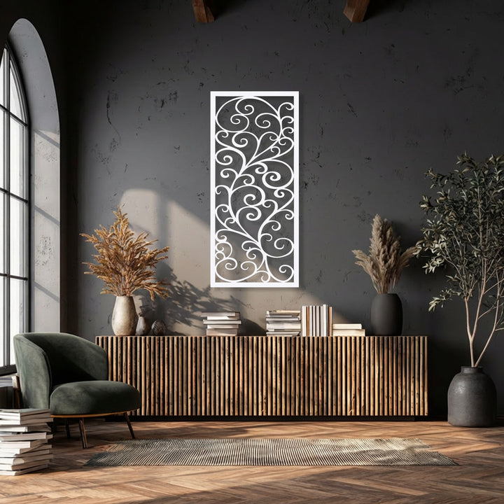 A plush dark green velvet armchair and stacked books on a rug foreground an elegant scroll pattern metal art for wall piece.