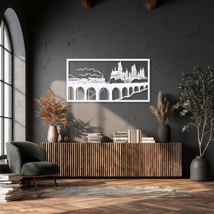 Strong diagonal sunlight and deep shadows dramatically illuminate the white metal wizard castle train scene decoration wall art on a dark textured wall.