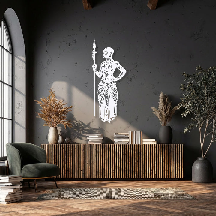 Focusing on the brightest area, a striking white metal art for wall depicts a Tribal African Warrior with a detailed spear on a dark wall.