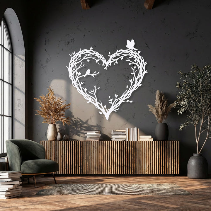 The radiant white bird & branch heart metal wall art, an intricate piece of decoration wall art, glows brightly against the dark textured wall.