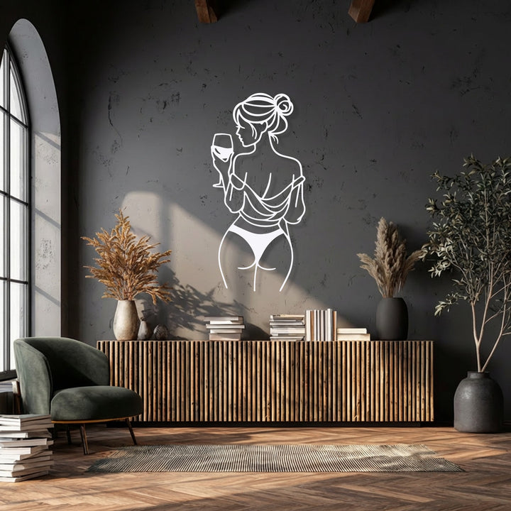 A plush dark green armchair and stacked books in the foreground provide a cozy setting for the elegant metal artwork.