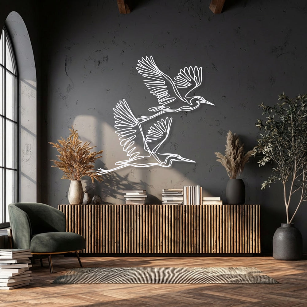 The negative space artfully outlines the minimalist flying herons metal wall art, creating striking decoration wall art against a dark wall.