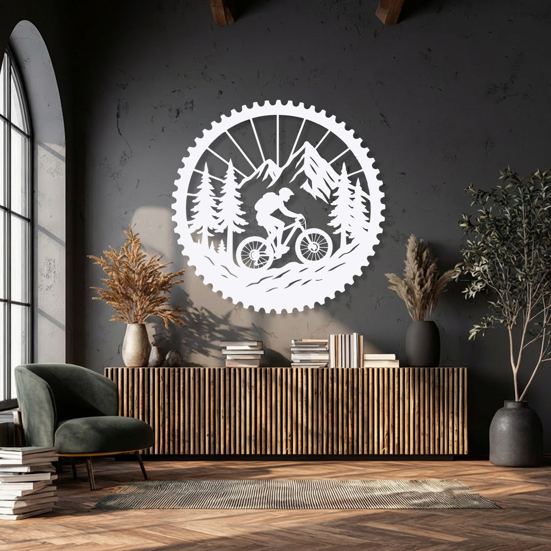 A white, intricate unique metal wall art piece depicting a mountain biker traversing a mountain and forest landscape within a cog outline.