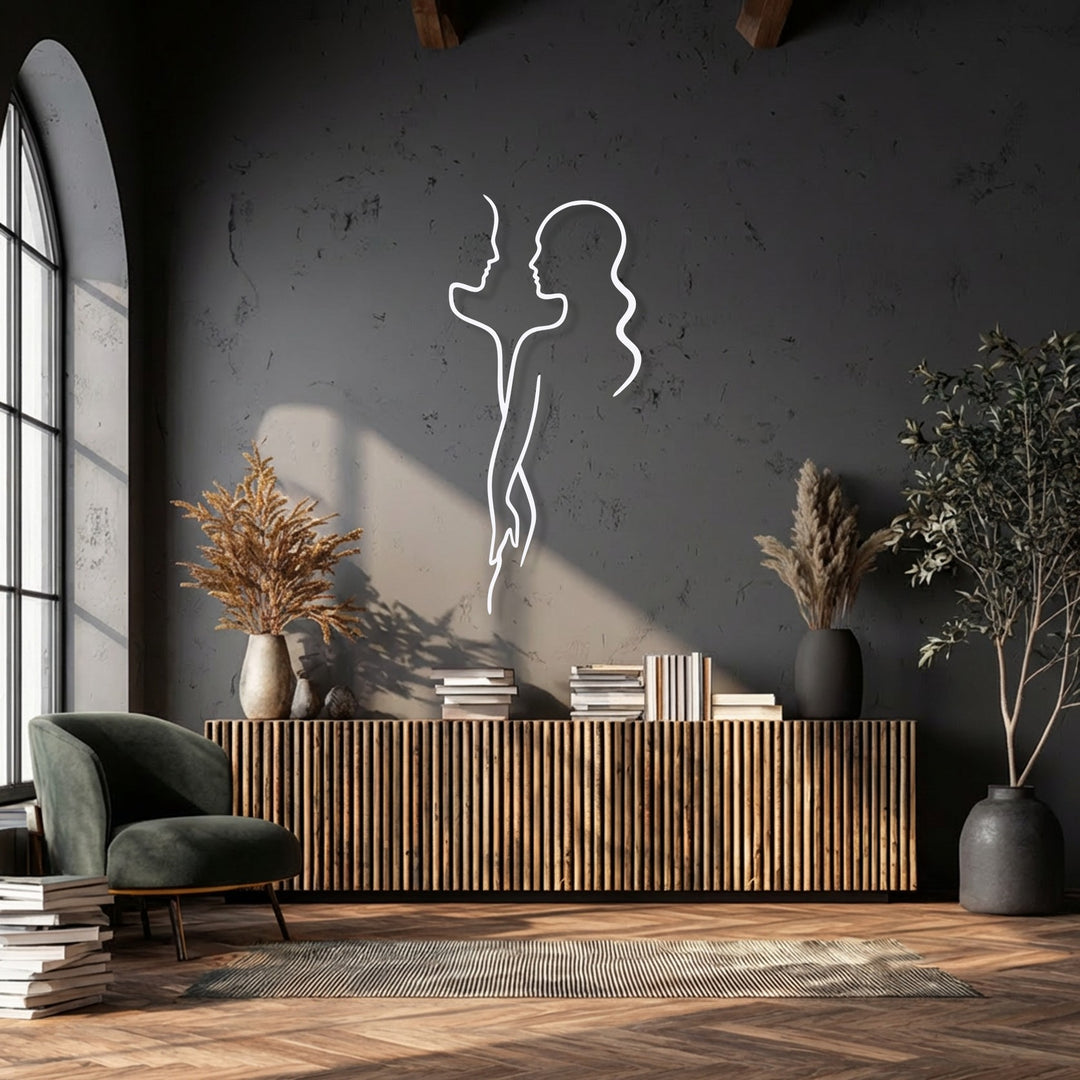 A minimalist white metal artwork of a couple is striking against the wall's color transition from sunlit gray to deep, shadowy charcoal.