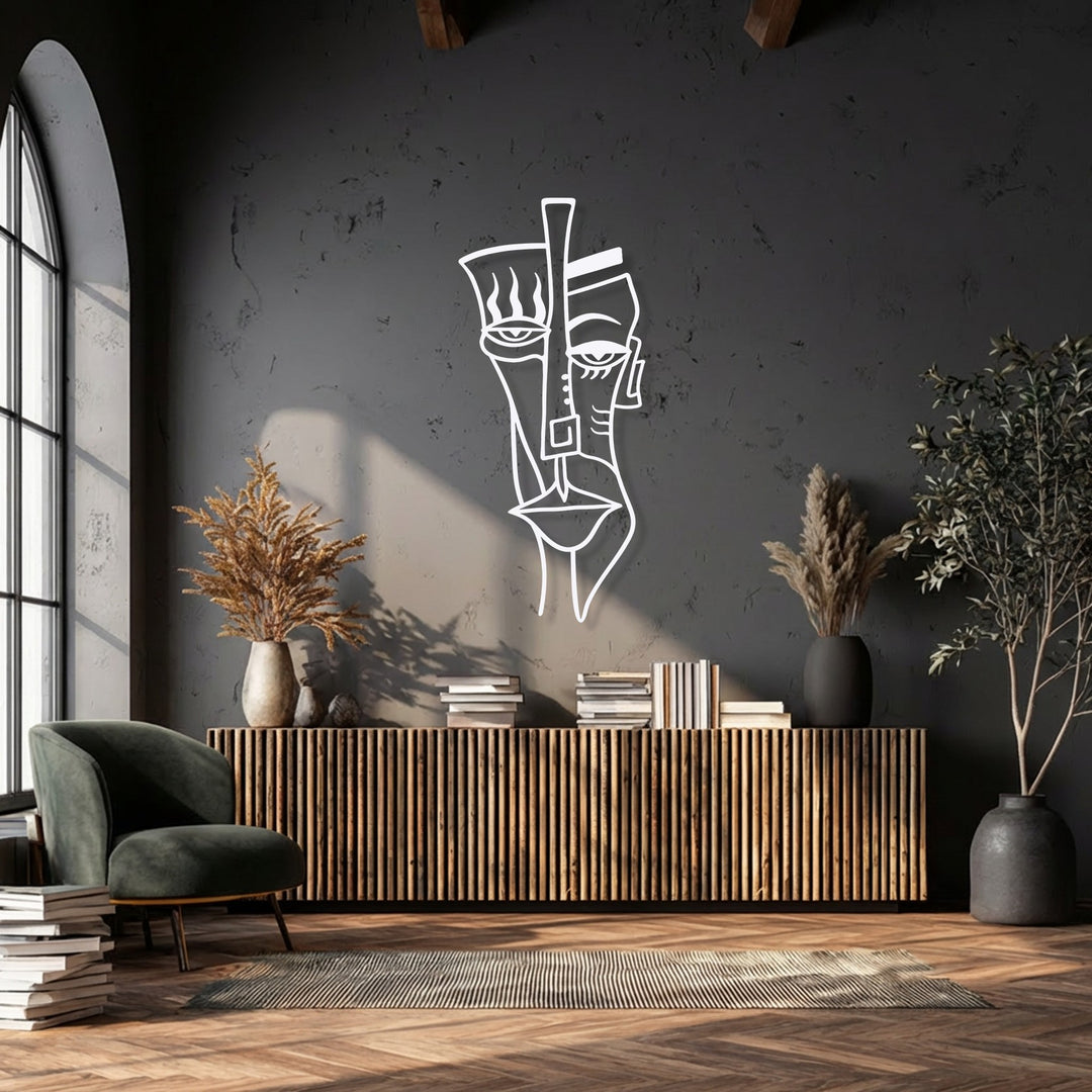 An intricate white abstract tribal face metal wall decor piece hangs prominently on a dark grey textured wall, above a wooden slatted console table.