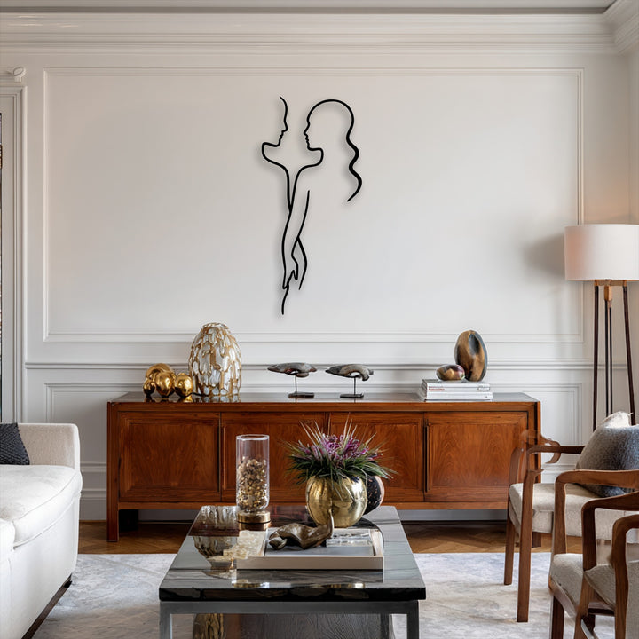 The stillness of a minimalist black metal decoration wall art depicting a couple's silhouette brings quiet elegance to a white paneled wall.