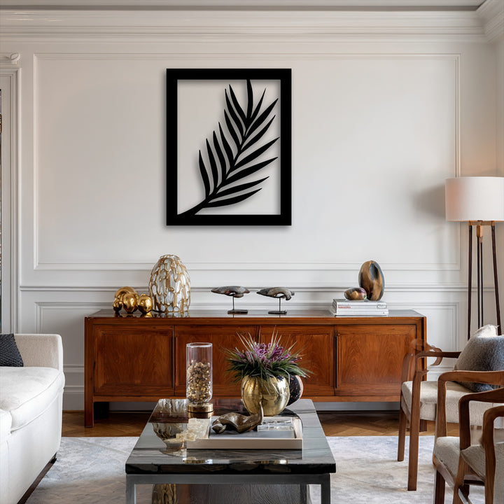 A vertically oriented rectangular piece of metal artwork features a striking minimal palm leaf silhouette within its frame.