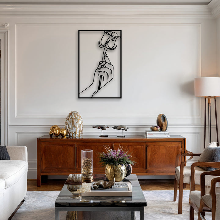The negative space of the white wall highlights the sleek design of the Minimalist Hand Holding Rose line art metal artwork.