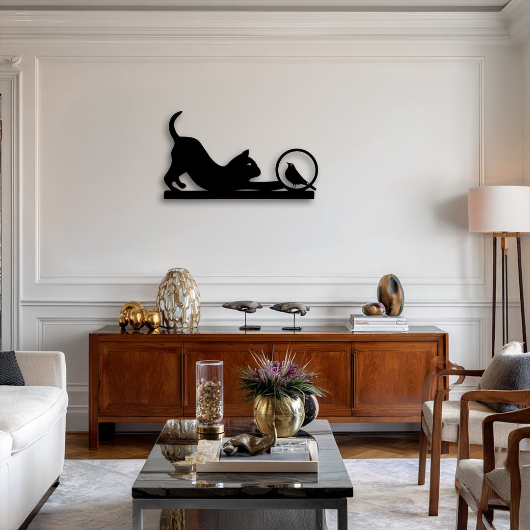 A horizontal, playful cat and curious bird silhouette metal wall decor features a stretching cat reaching for a bird in a circular design.