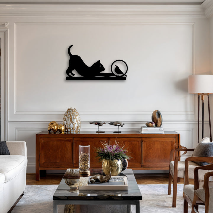 A horizontal, playful cat and curious bird silhouette metal wall decor features a stretching cat reaching for a bird in a circular design.