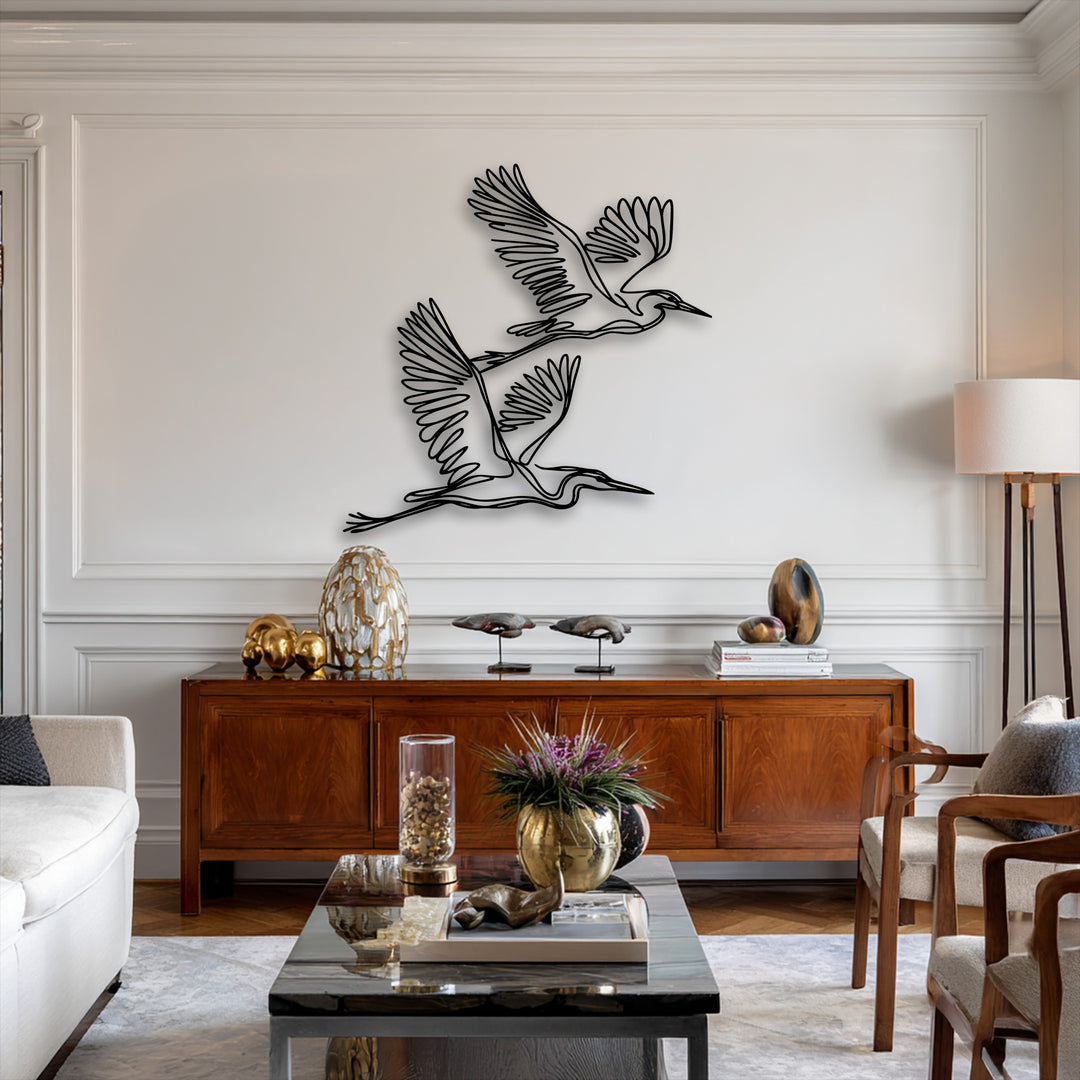Two large, graceful minimalist flying herons metal wall decor pieces are prominently displayed on a white wall above a rich wooden console.