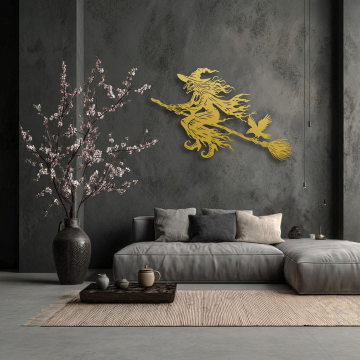 Horizontally oriented decorative metal art captures a dynamic golden silhouette of a flying witch on a broom with a crow.