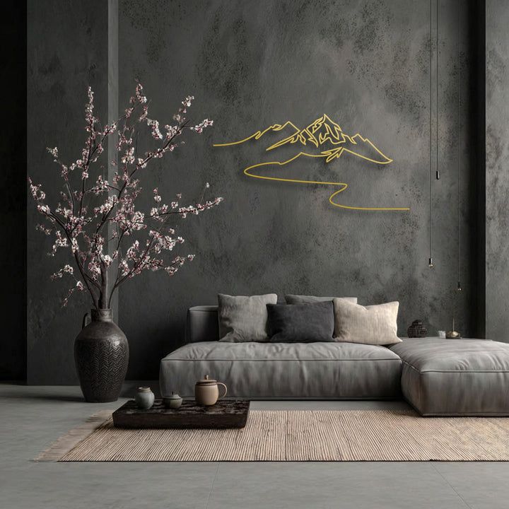 The serene mood of a minimalist living space is enhanced by the modern mountain line metal artwork and a delicate blossoming tree.