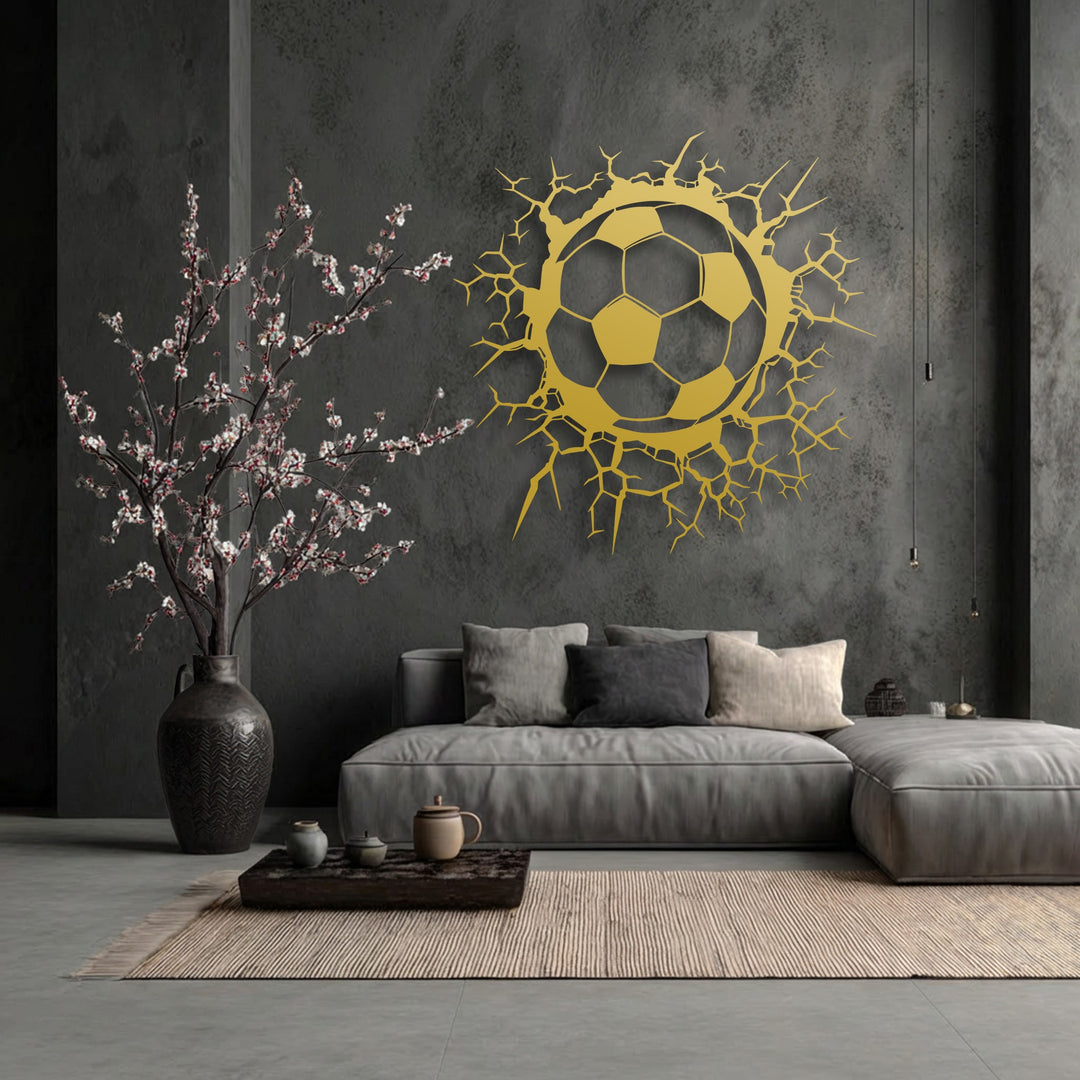 The deep negative space of the textured dark wall dramatically frames the golden breaking wall soccer ball decorative metal art.
