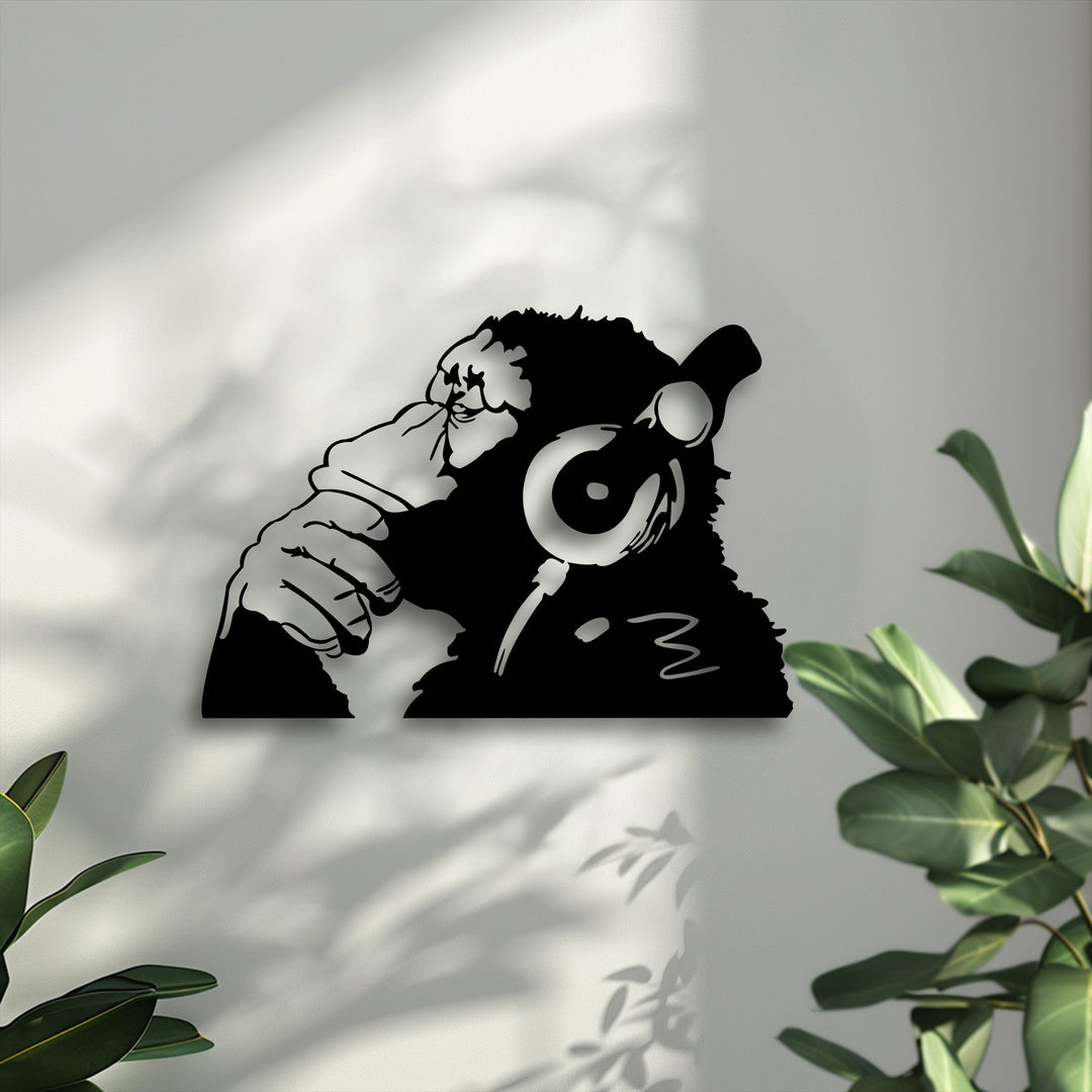 A striking black silhouette of an urban monkey with headphones, hand to face, as unique metal wall art against a textured grey wall.