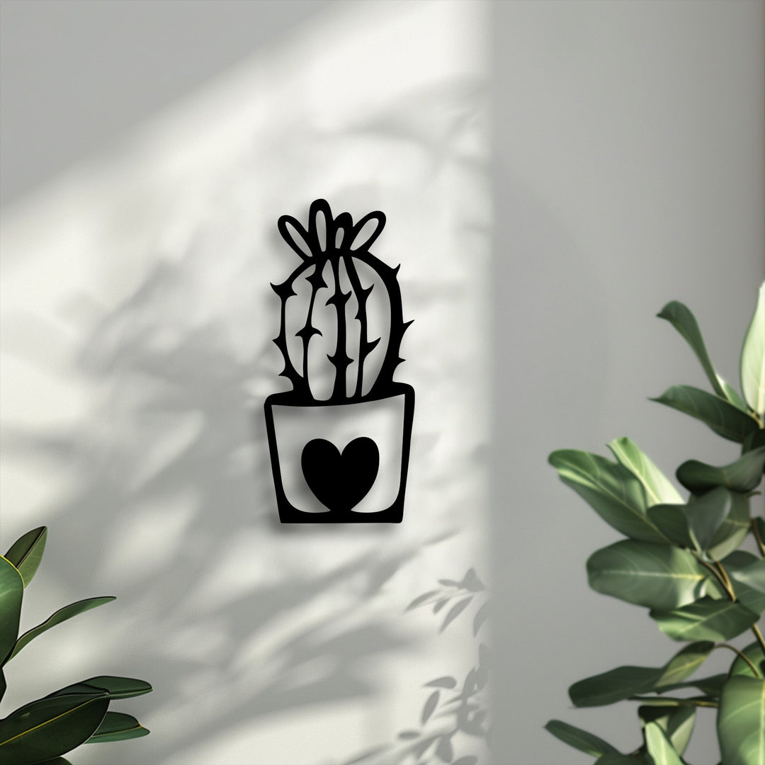 Intricate negative space on a textured white wall frames a black decorative metal art piece, depicting a minimal cactus with a heart pot design.