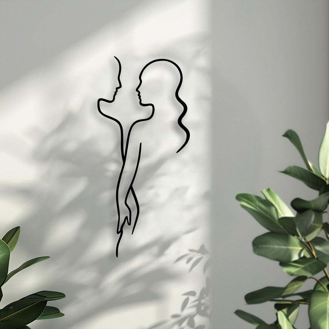 The foreground features vibrant green plant leaves, elegantly framing the minimal couple line unique metal wall art.
