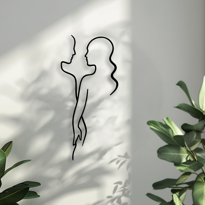 The foreground features vibrant green plant leaves, elegantly framing the minimal couple line unique metal wall art.
