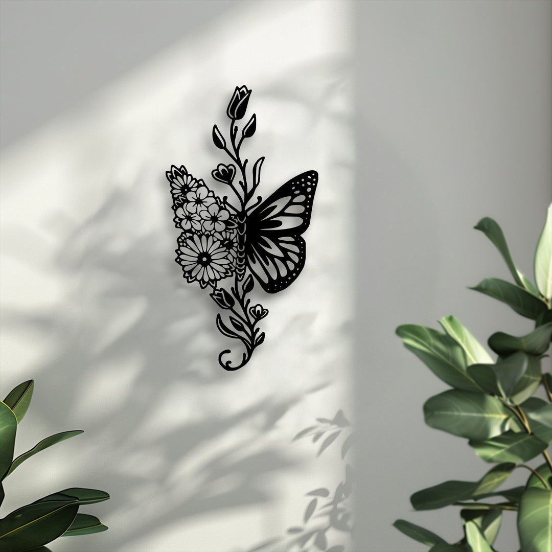 Lush green leaves frame the foreground, highlighting the intricate black metal artwork of a butterfly and delicate floral design.